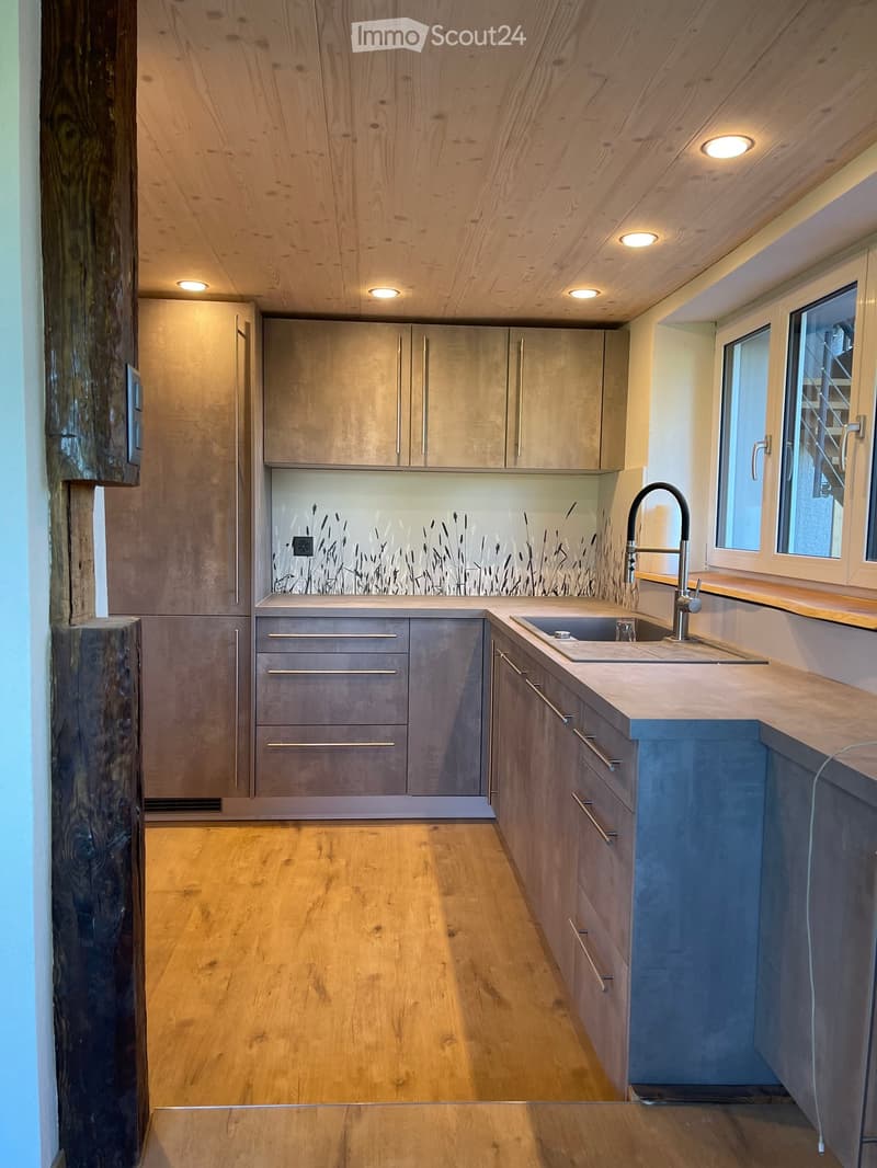 Modern kitchen with wooden ceiling, light wood flooring, stainless steel sink, and grey cabinets.
