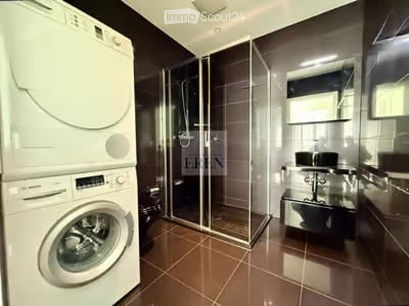 Modern bathroom with a washing machine, glass-enclosed shower, sink, and mirror.
