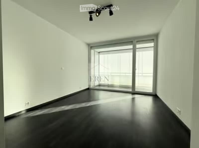 Empty room with white walls, dark wooden floor, large sliding glass doors leading to a balcony.