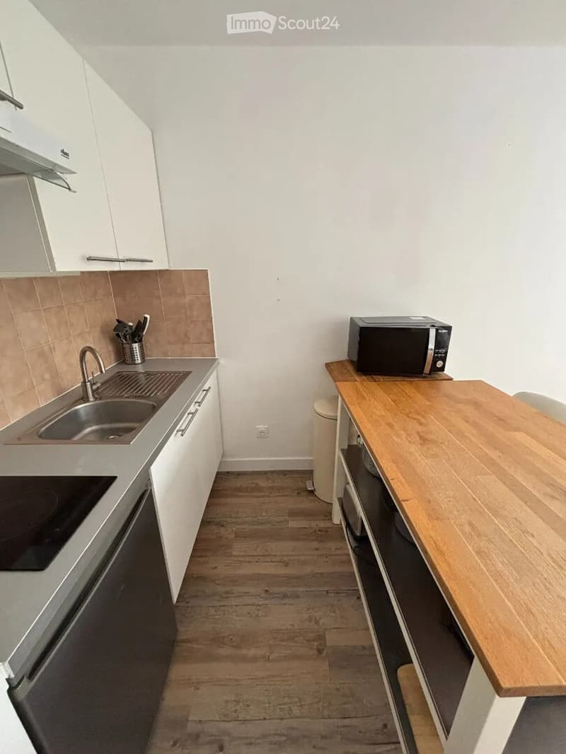 Modern kitchen with white cabinets, wooden table, microwave, sink, and stove.