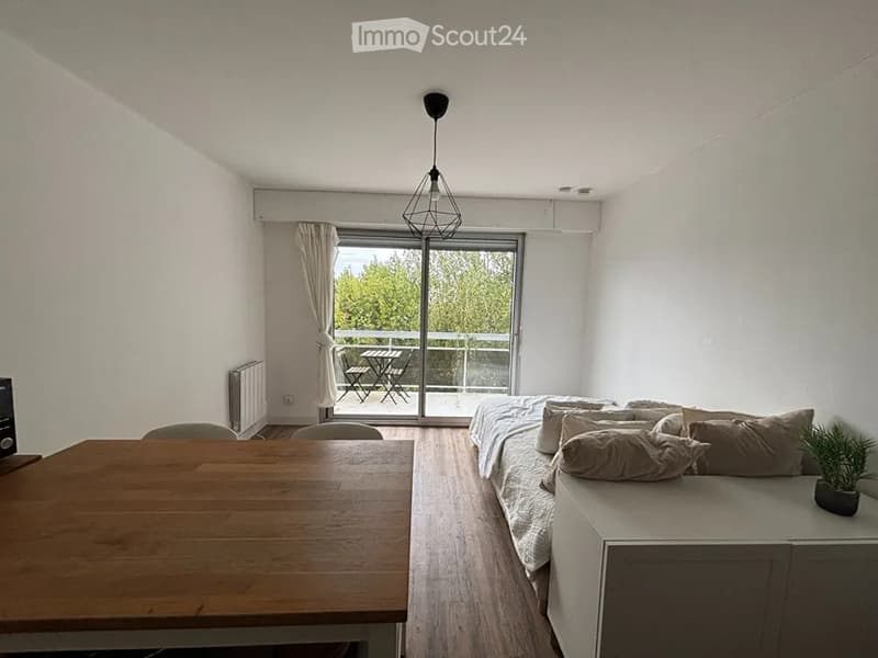 Cozy studio with a bed, sofa, dining table, chairs, and a small balcony with outdoor furniture.