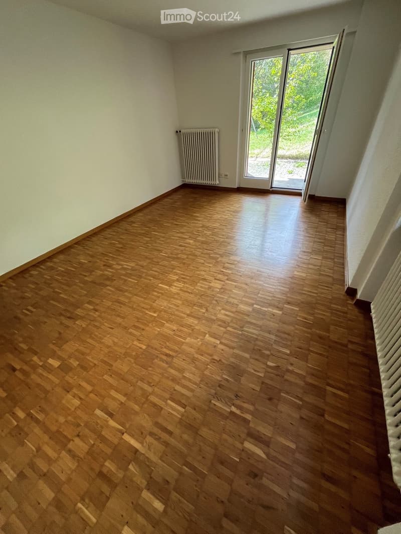 Empty room with wooden flooring, white walls, and a sliding glass door leading to an outdoor area.