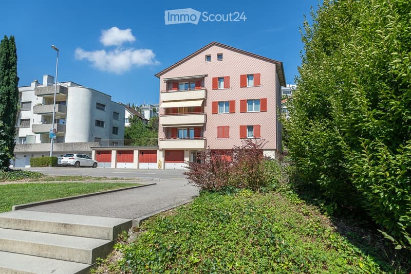 multistory building with multiple garages, red doors, balcony, car parked in front, multiple windows