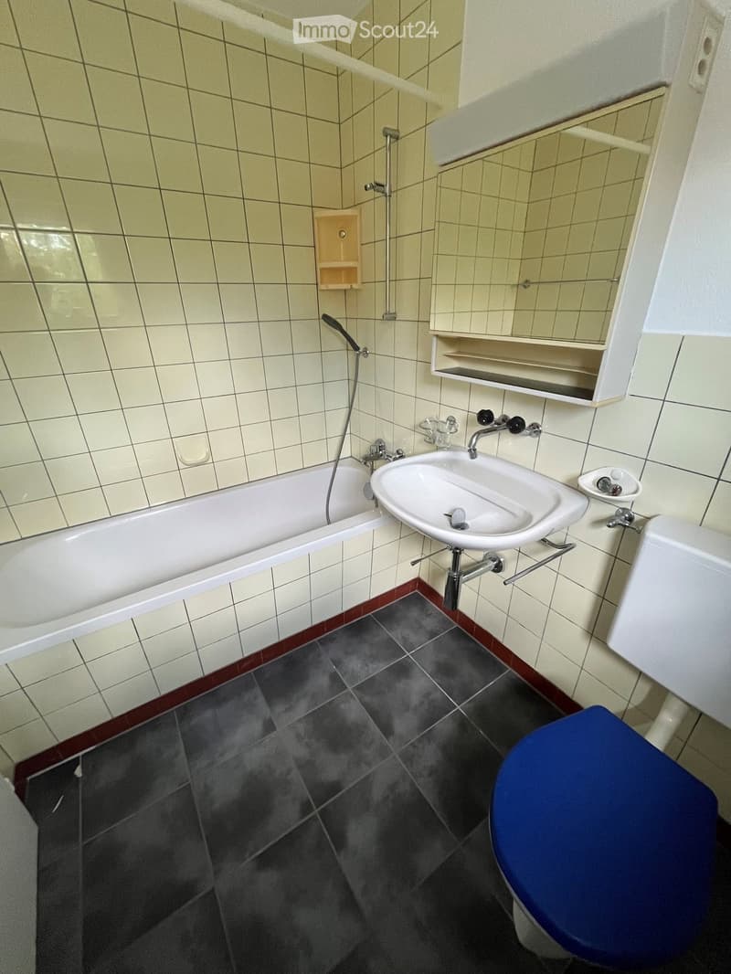 Bathroom with a bathtub, sink, toilet, and mirror. The walls are tiled, and the floor has dark tiles with a red border.