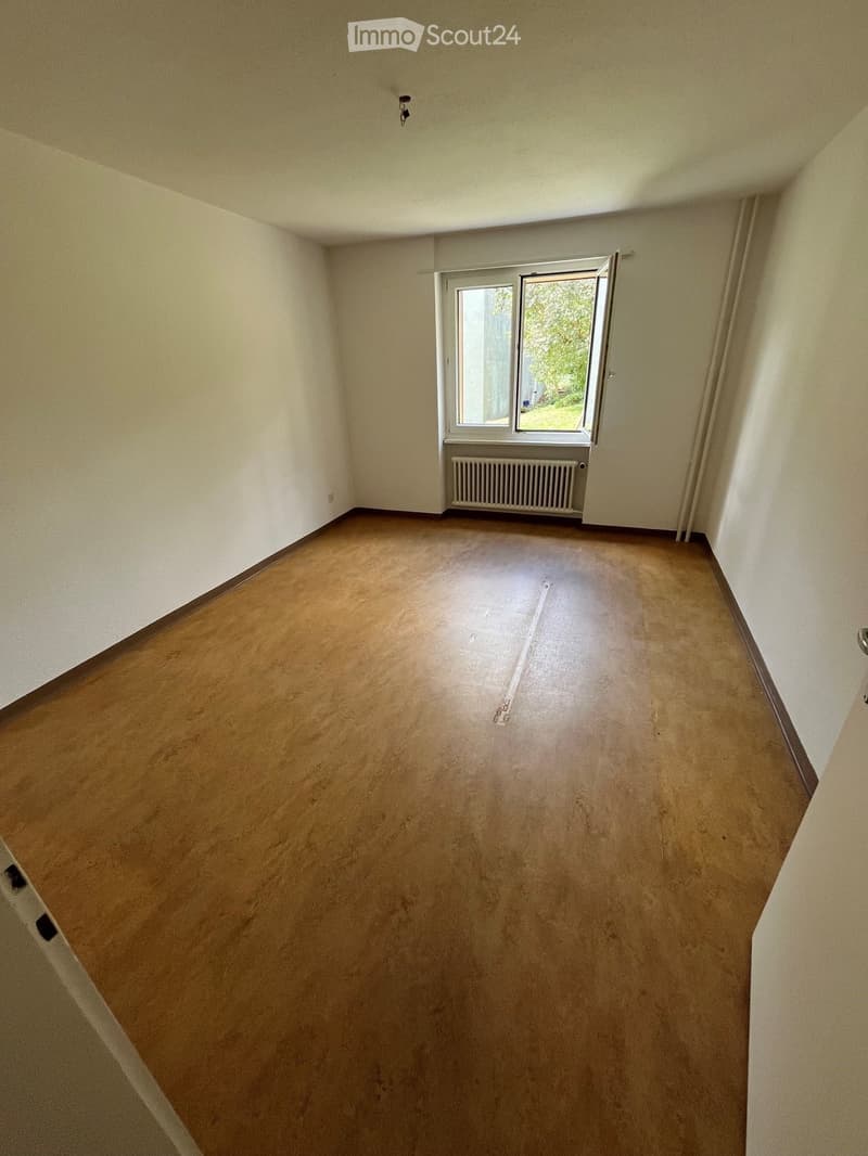 Empty room with wooden flooring, white walls, and a window with a radiator below it.