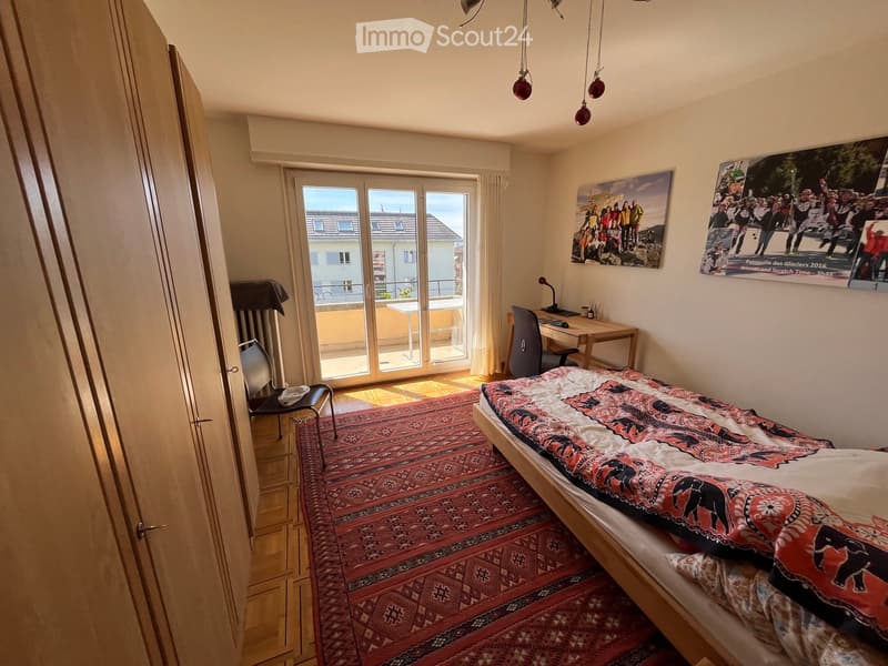 Cozy bedroom with a single bed, desk, chair, and a view through large glass doors to a balcony.