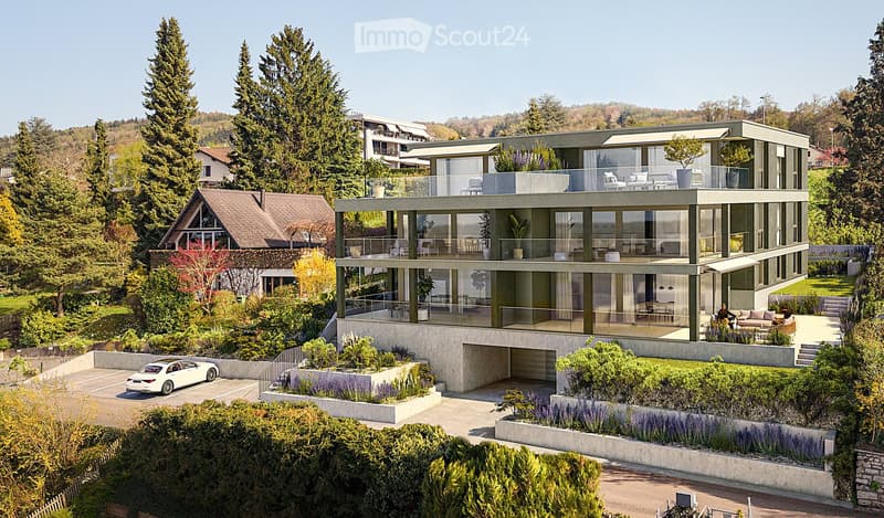 Modern two-story house with large glass windows, balconies, and a landscaped garden. Features include a raised ground floor, garage, and parking area.