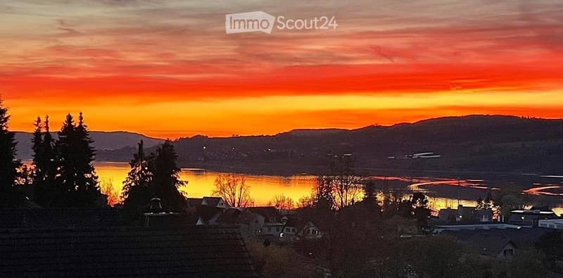 Scenic view of a lake at sunset with mountains in the background and houses on the shore.