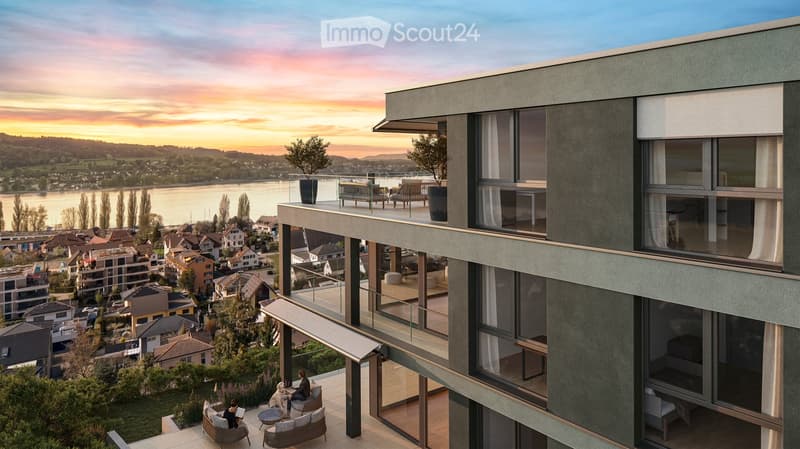 Modern balcony with large windows, overlooking a scenic river view, featuring outdoor seating and potted plants.