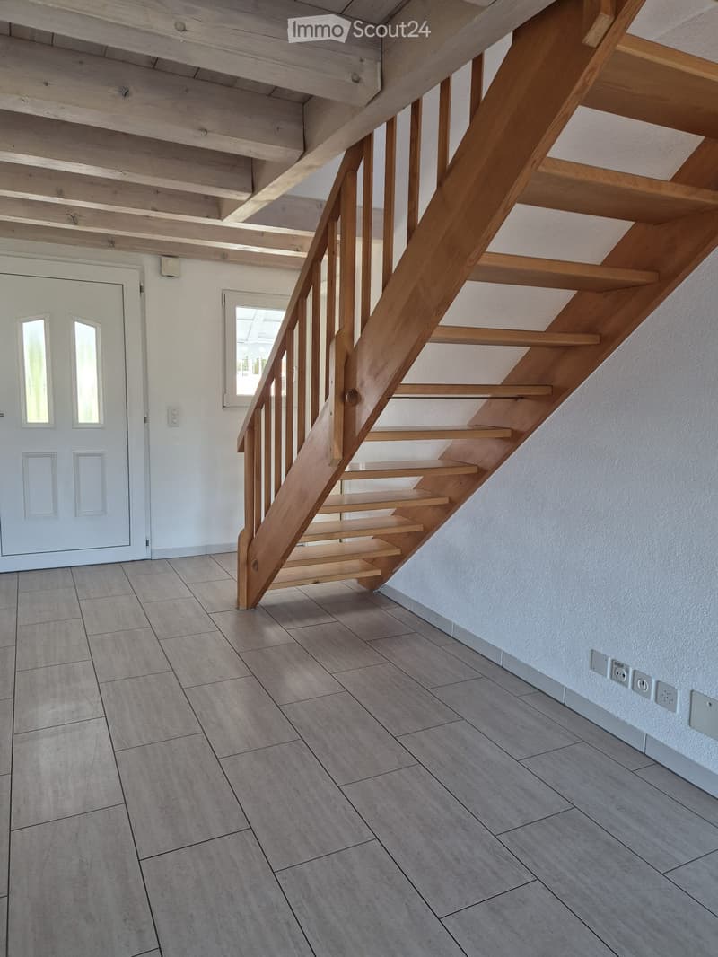 Modern hallway with wooden staircase, tiled floor, white walls, and a white door with glass panels.