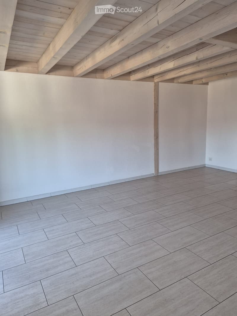 Empty room with light-colored wooden flooring and white walls, featuring exposed wooden beams on the ceiling.