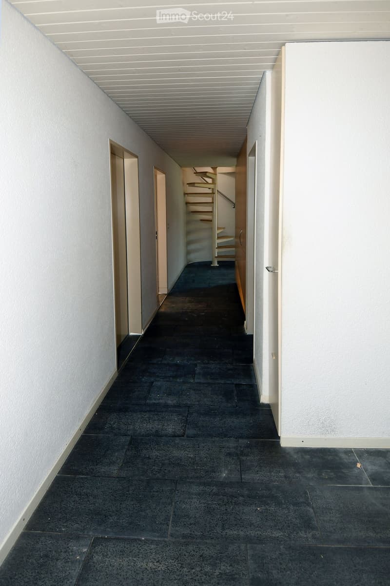 Empty hallway with white walls, black tiles on the floor, wooden spiral staircase, and two doors