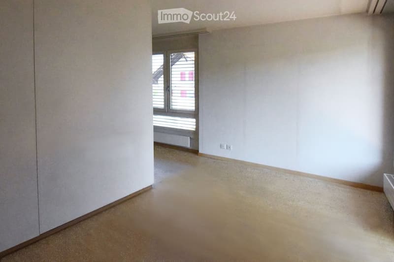 an empty room with white walls and beige floor, a window with blinds, a power outlet on the wall