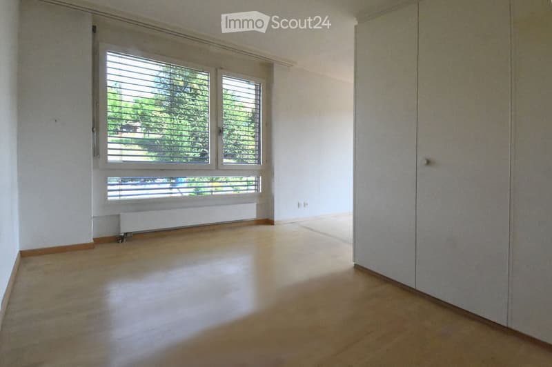 Empty room with large window, wooden floor, and wardrobes