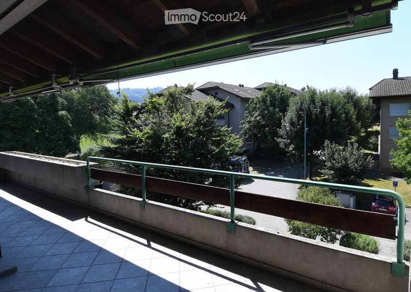 Balcony with metal railing and concrete flooring, overlooking a parking lot and greenery.