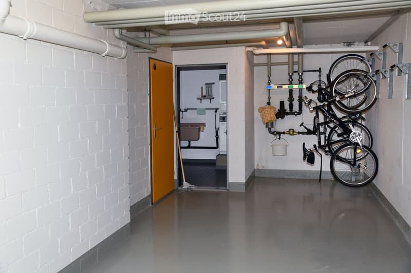 Underground room, white brick wall, gray floor, washing machines, bicycles
