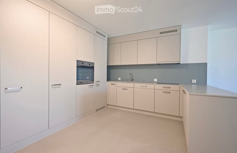 Modern, minimalist kitchen with light-colored cabinets, a central island, and a sink with a faucet.