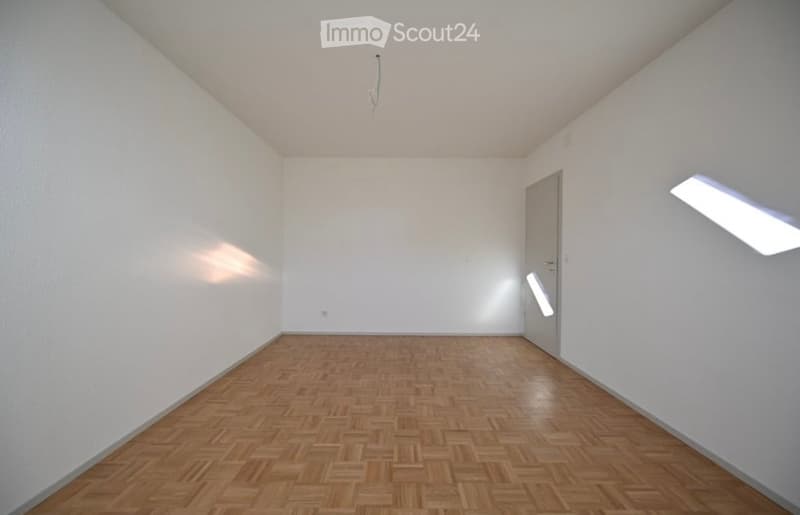 Empty room with wooden parquet flooring, white walls, and a single door. No furniture or equipment is present.