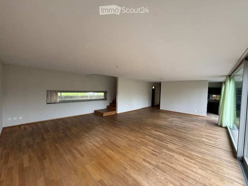 Completely empty room with wooden flooring, large windows, and a small staircase leading to another level.