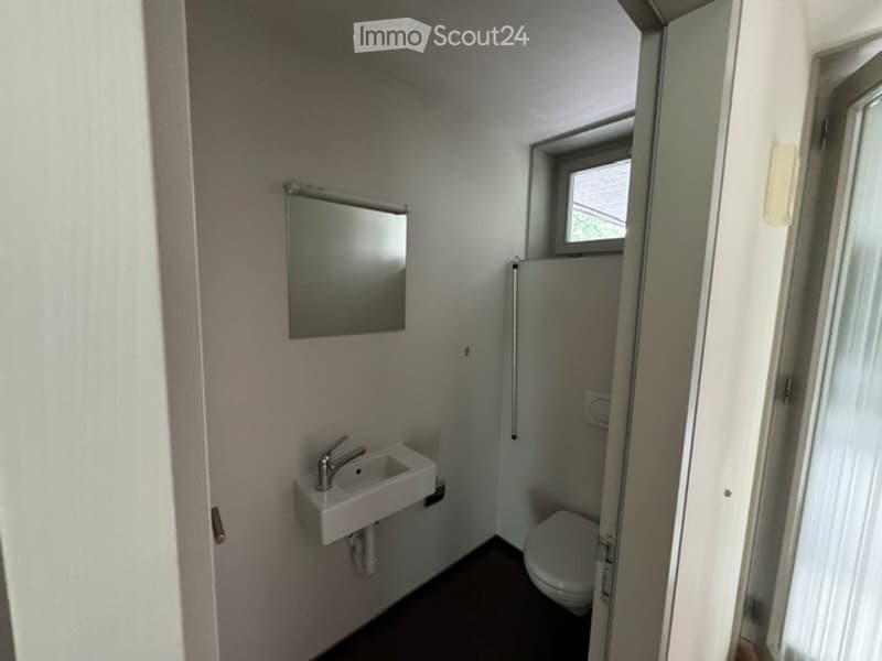 Compact bathroom with a white sink, chrome faucet, mirror, and toilet. Small window provides natural light.