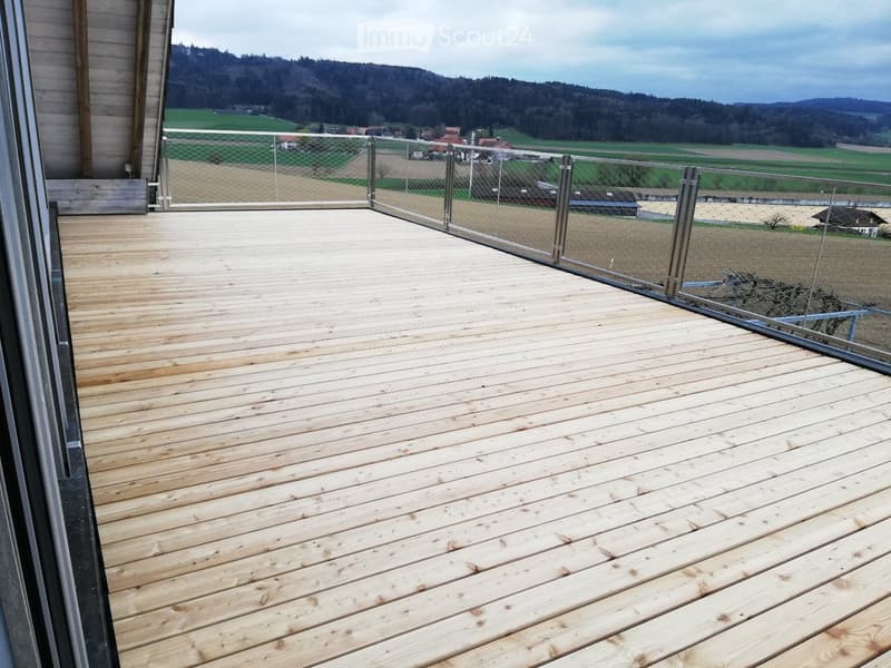 Wooden deck with metal railing, overlooking a rural landscape with fields and hills.