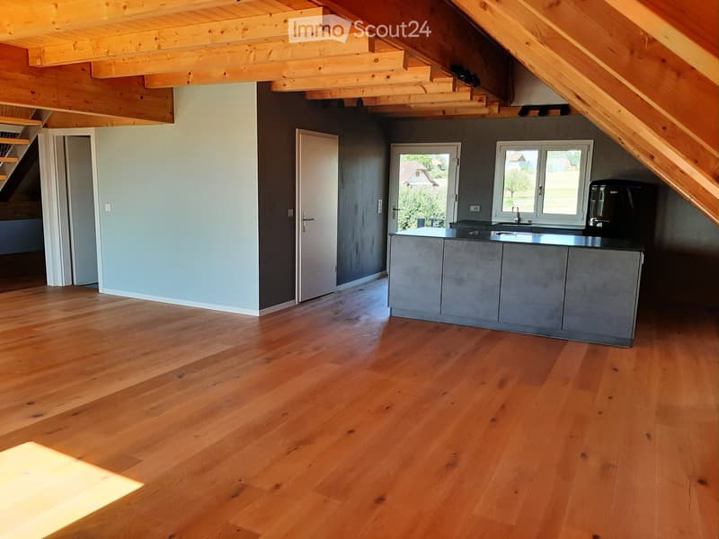 Modern kitchen with wooden flooring, grey cabinets, and a kitchen island. Features a sink, faucet, and a coffee machine.