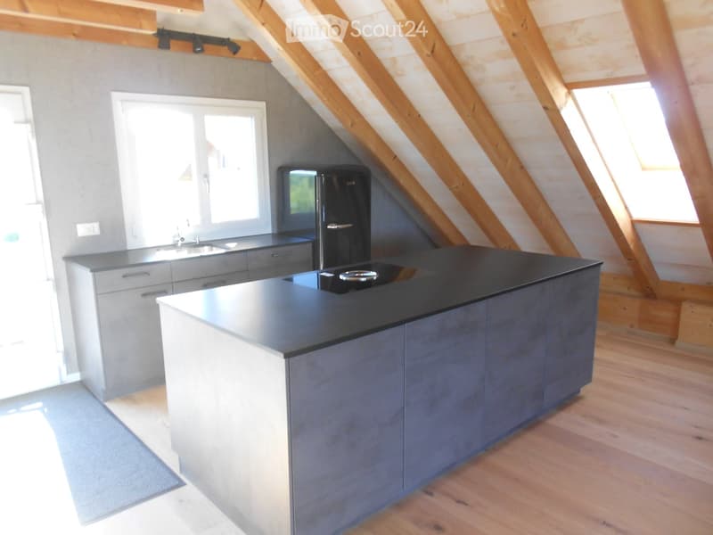Modern kitchen with grey cabinets, a central island, and a black countertop, featuring wooden beams and skylights.