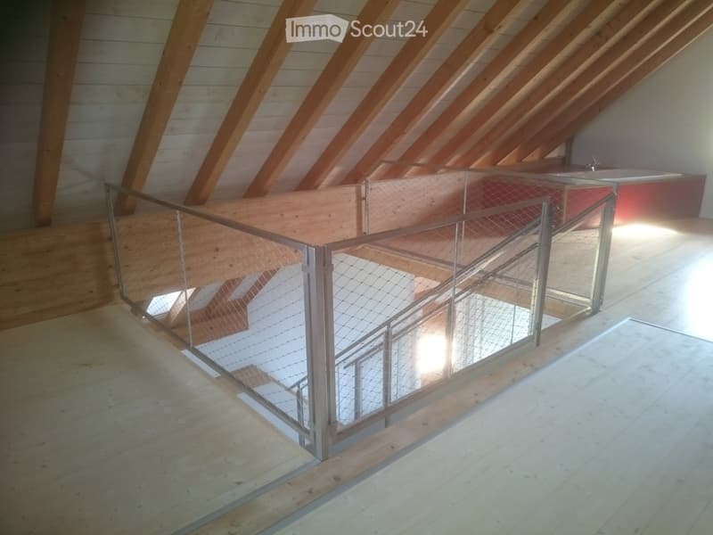 Open, airy hallway with wooden beams and a modern metal railing leading to a staircase, featuring exposed wooden beams and natural light.