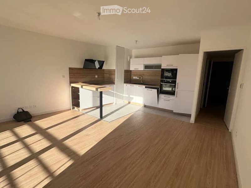 Modern kitchen with white cabinets, wooden countertop, built-in oven, dishwasher, and a small screen on the counter. The floor is light wood, and the space is well-lit with natural light.