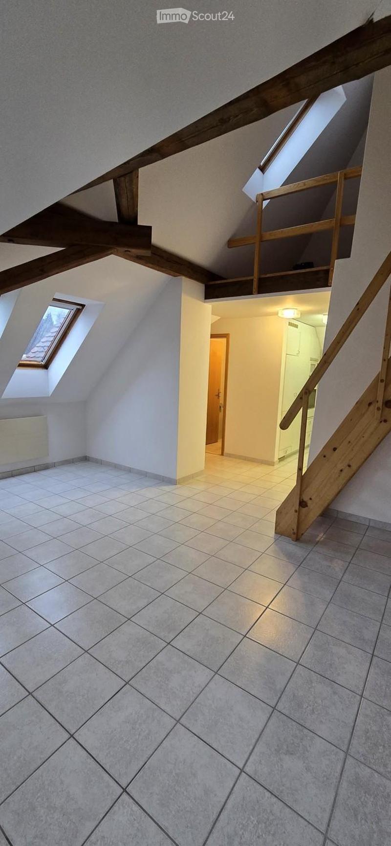 Empty attic space with exposed wooden beams, tiled floor, and skylight windows. Staircase leads to another level.