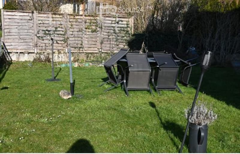 A grassy backyard enclosed by wooden fencing, with several black folding chairs and tables arranged on the lawn, along with a small decorative plant in a pot.