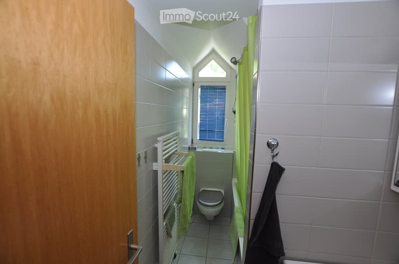 Modern bathroom with grey tiles, a toilet, a sink, a towel rack with green towels, and a shower curtain.