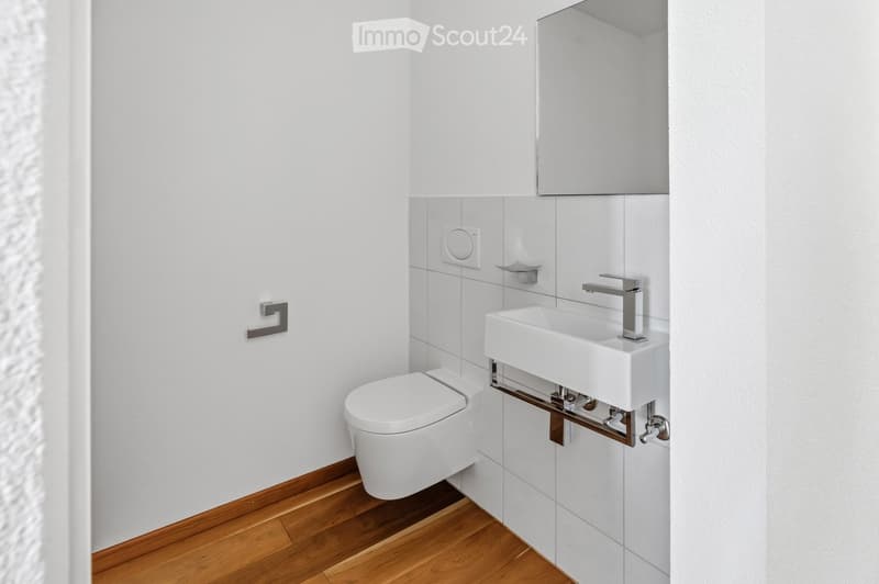 Modern bathroom with white tiled walls, wooden flooring, a toilet, a sink with a modern faucet, and a mirror above the sink.