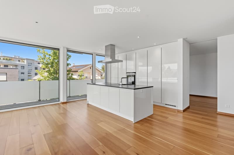 Modern kitchen with white cabinets, a central island, and large windows overlooking a green area.