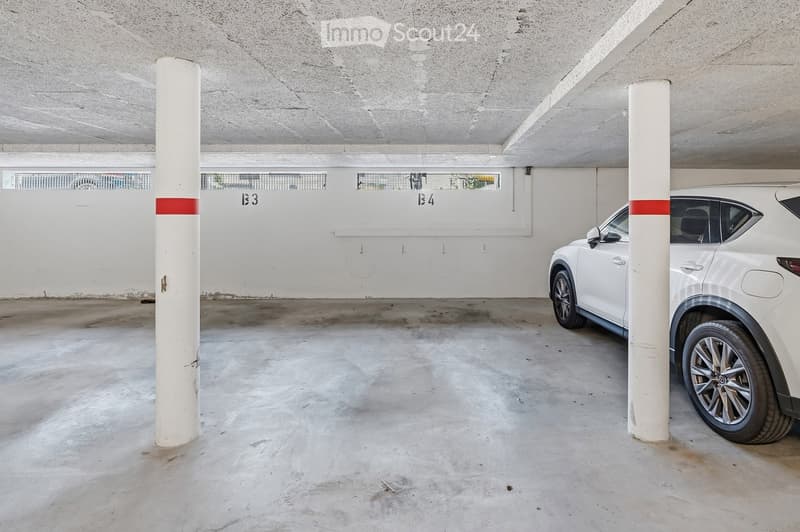Underground parking area with concrete floor and walls, white support pillars, and a white SUV parked in one of the spaces.