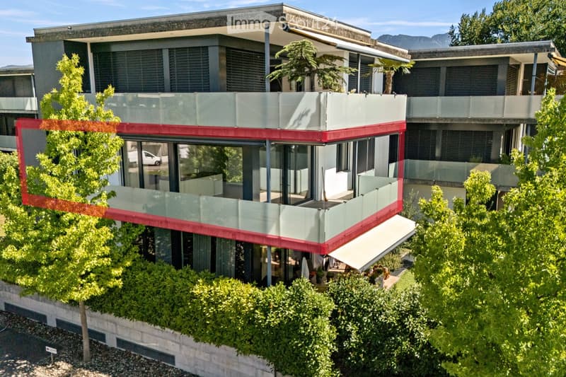 Modern two-story building with large windows, balconies, and contemporary design, surrounded by greenery and trees.