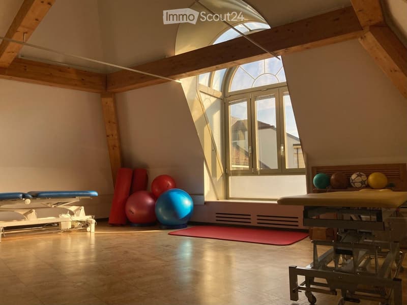A large room with exercise equipment, a large window, and wooden beams.