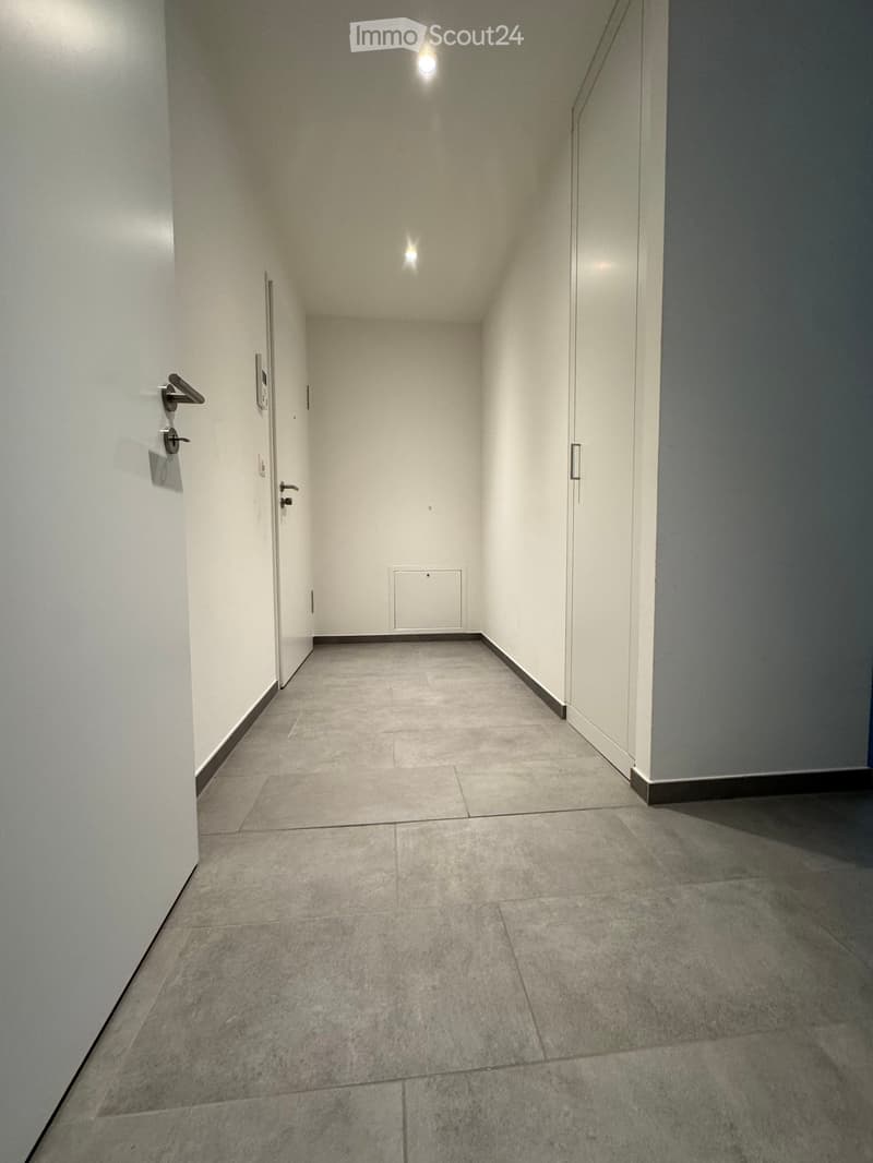 Empty hallway with tiled floor, white walls, and recessed lighting. Doors visible on both sides.