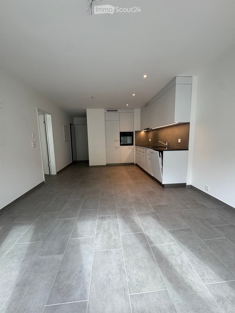 Empty kitchen area with white cabinets, stainless steel appliances, and grey tiled flooring.