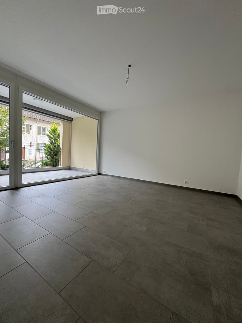 Empty room with tiled floor, large sliding glass door leading to balcony, white walls, and visible electrical outlet.