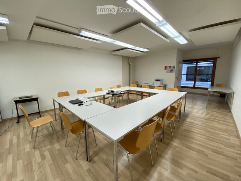 Bright meeting room with white tables, orange chairs, and a projector, arranged around a central table.