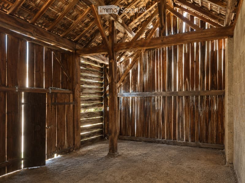 Empty wooden barn interior with exposed beams, wooden doors, and natural light filtering through gaps in the walls.