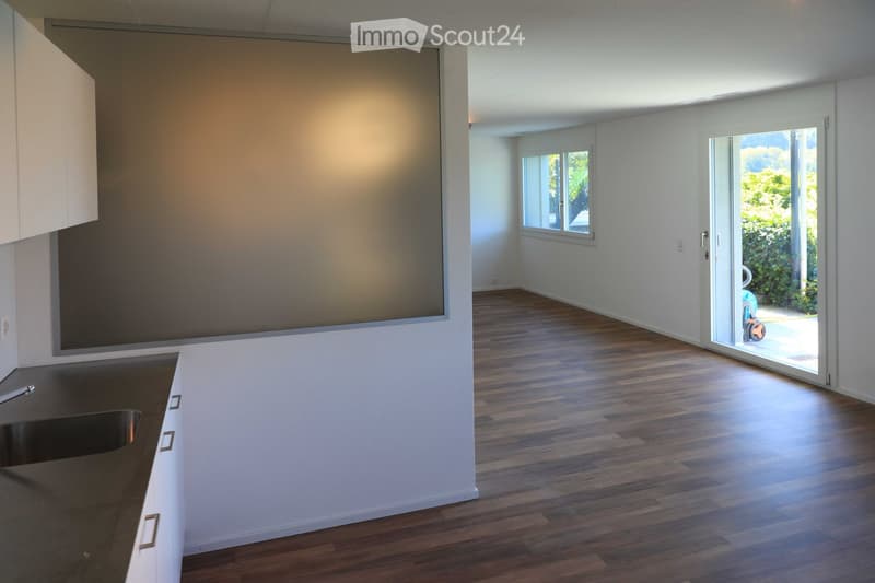 Empty room with wooden flooring, white walls, and large windows, including a sliding glass door leading outside.