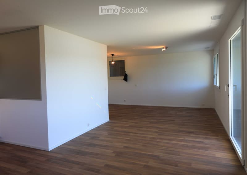 Empty room with wooden flooring, white walls, and large windows allowing natural light. No furniture or personal items are present.