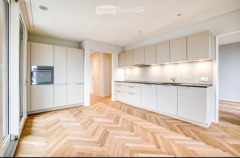 Modern kitchen with white cabinets, herringbone wooden flooring, and built-in appliances including an oven and sink.
