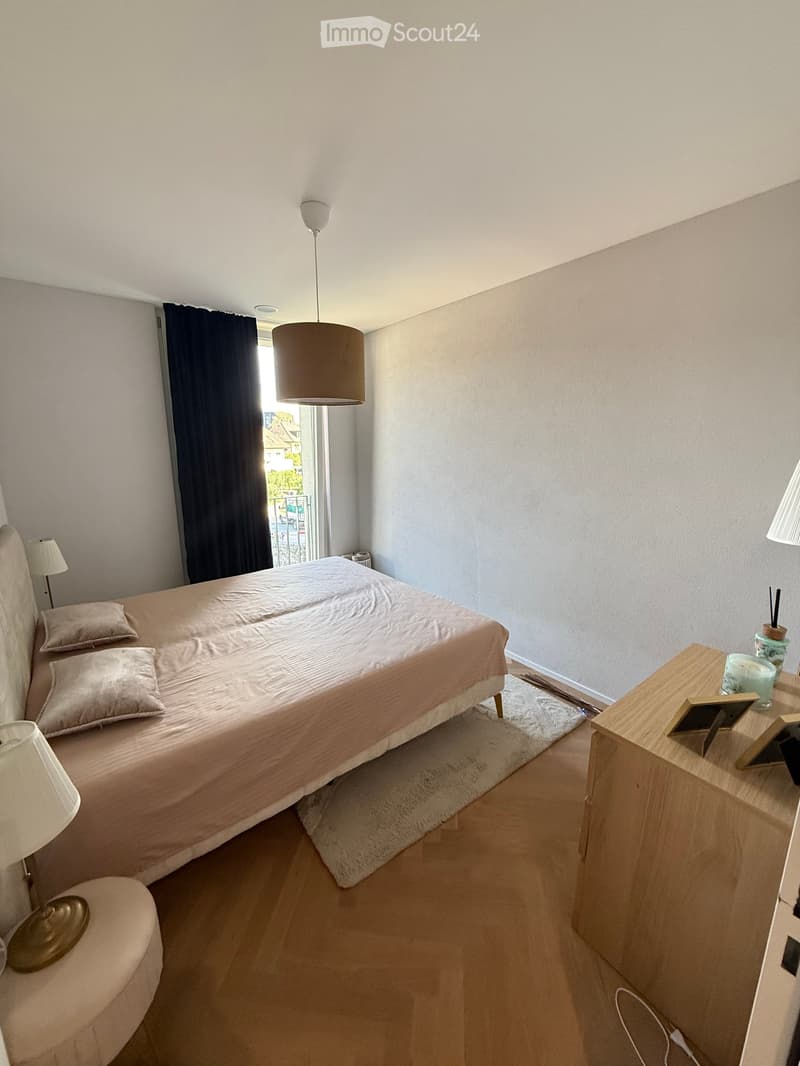 A modern bedroom with a double bed, nightstands, lamps, and a small table with decorative items.