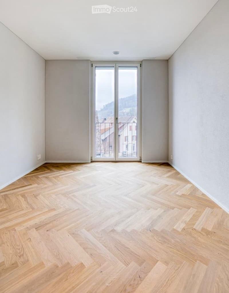 Empty room with light wooden flooring and large glass sliding doors leading to a balcony.