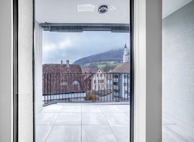 Balcony with tiled floor, metal railing, and scenic view of a town with houses and a church tower.