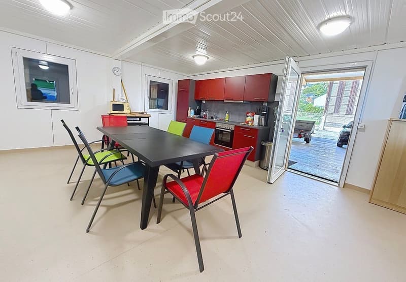 Bright room with a black dining table surrounded by colorful chairs, red cabinets, and a microwave on a counter.