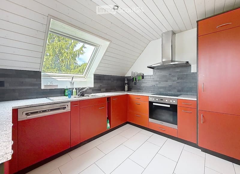 Modern kitchen with red cabinets, white countertops, stainless steel appliances, and a large skylight window offering a view of greenery.